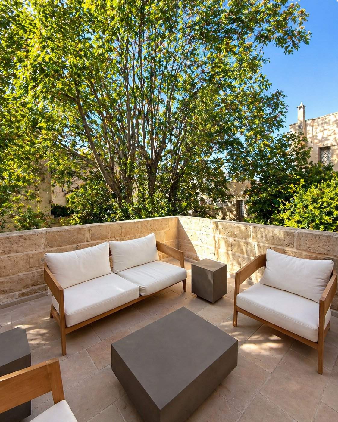 The sunlit rooftop terrace at Palazzo Zimara, Lecce, with teak-framed cream-cushioned lounge furniture, concrete cubic tables, and views over the carparo limestone walls and historic-center skyline of Lecce's Baroque old town
