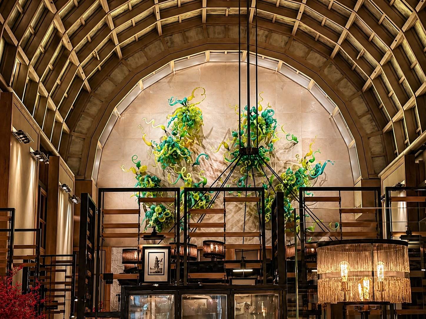 The vaulted lobby at The Ritz-Carlton, Millenia Singapore, with the iconic Dale Chihuly green and yellow blown-glass sculpture suspended beneath Kevin Roche's arched timber ceiling