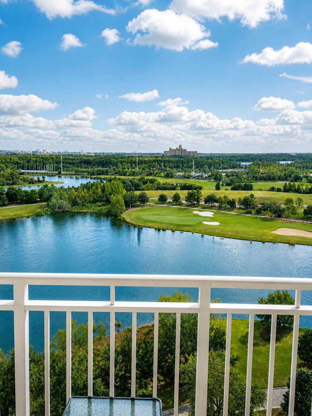 The view from a high-floor balcony at The Ritz-Carlton Orlando, Grande Lakes, looking south across the resort lake to the Greg Norman-designed Ritz-Carlton Golf Club championship course, with the sibling JW Marriott Orlando, Grande Lakes visible on the far side of the 500-acre property